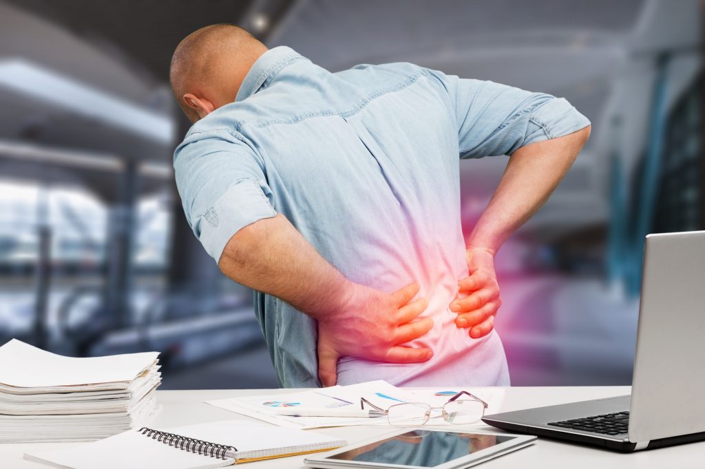 Man suffering from back pain at work at his desk, representing Pain Relief Chiropractor Pinellas Park.